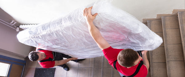 Two men from a moving company carrying a mattress up stairs