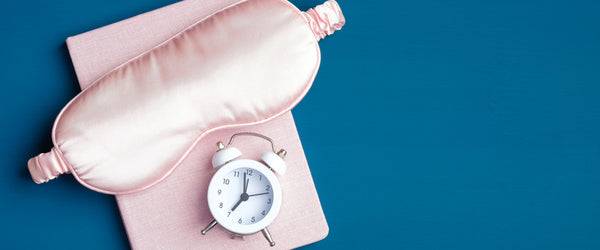 Pink eye mask and small alarm clock on a pink journal.