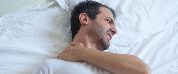 Man in bed holding neck due to neck pain while sleeping